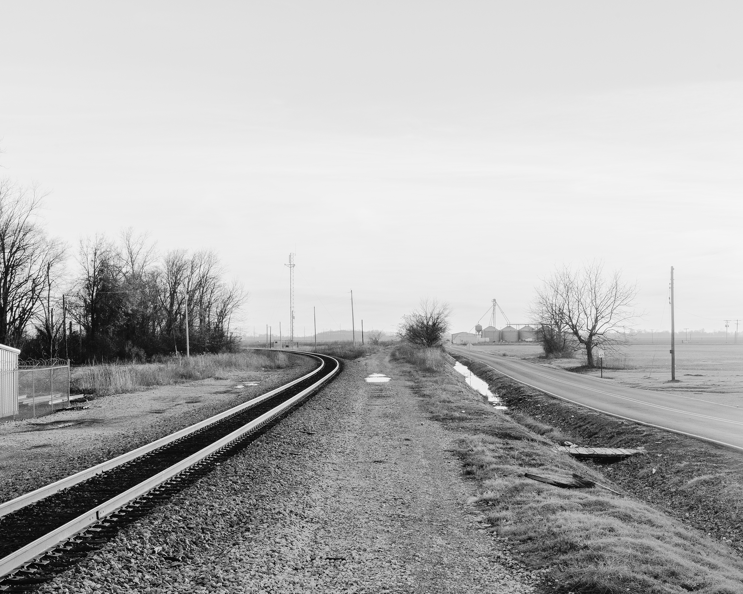 Black and white photograph of a landscape with a railroad track and a road.