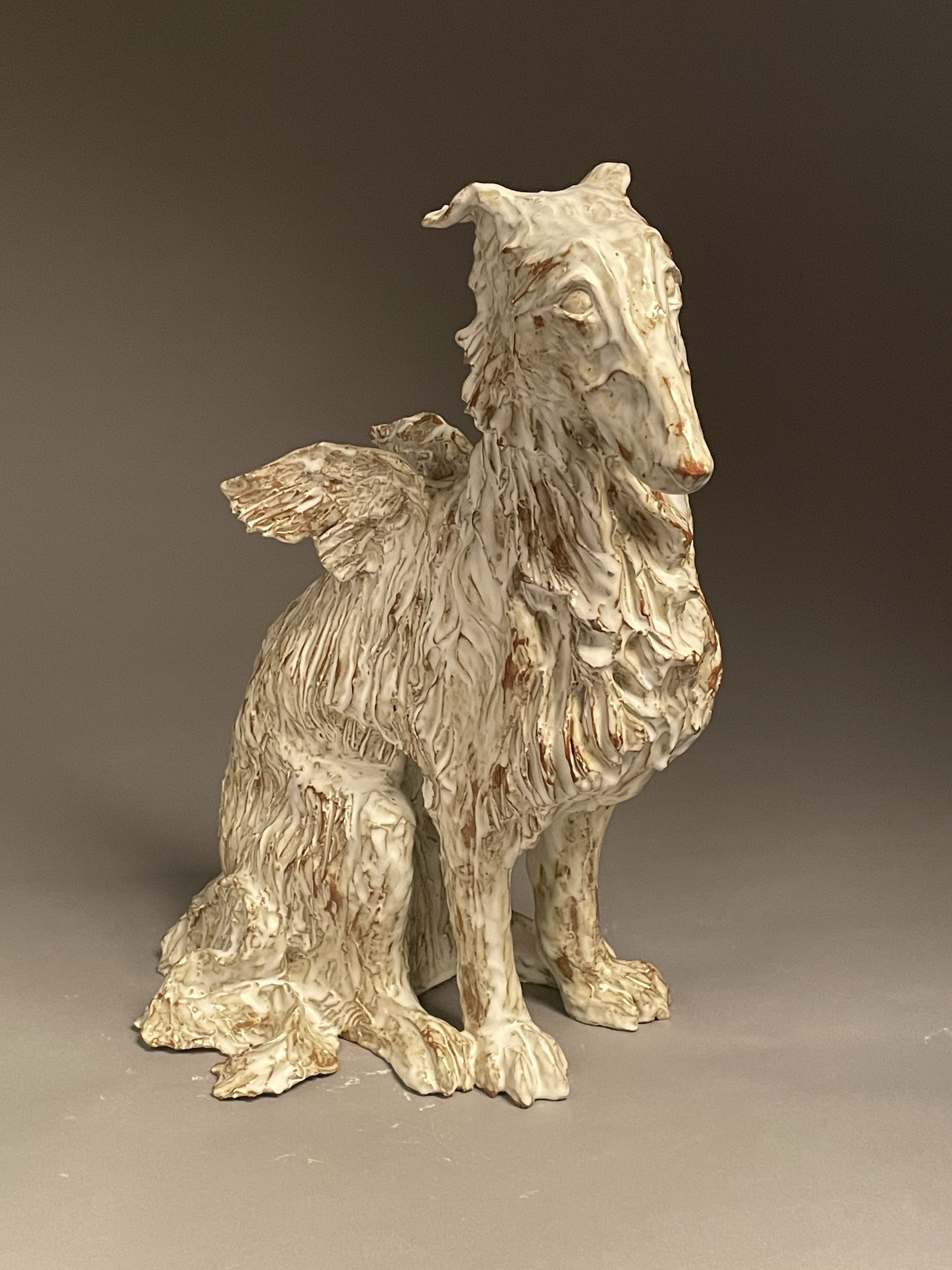 Ceramic dog sculpture with small feathered wings sitting looking forward with a white glaze