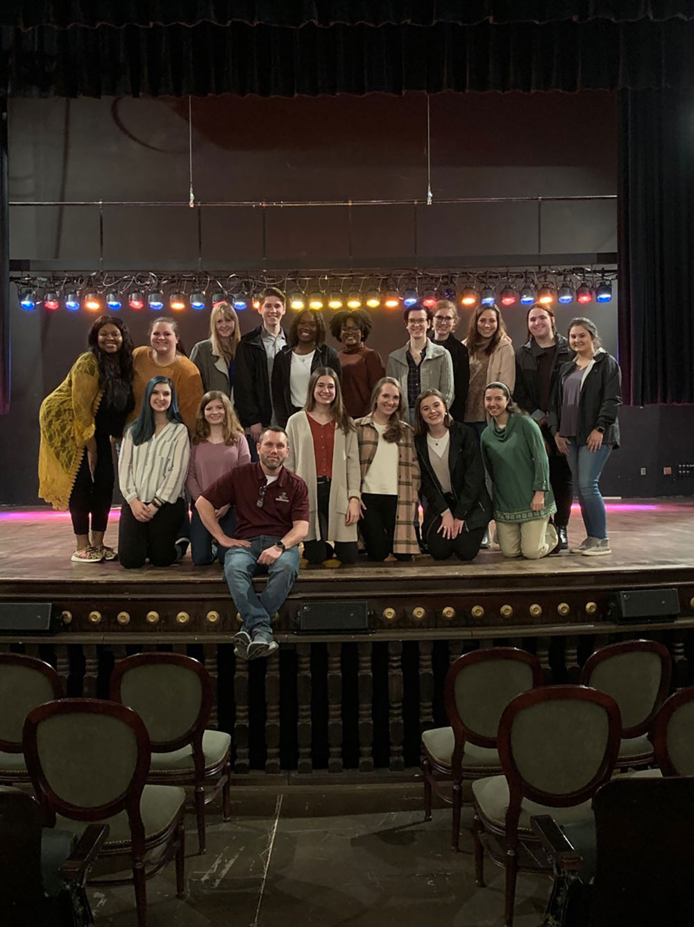 a group of students in the lighting class on stage with a row of colorful lights behind them