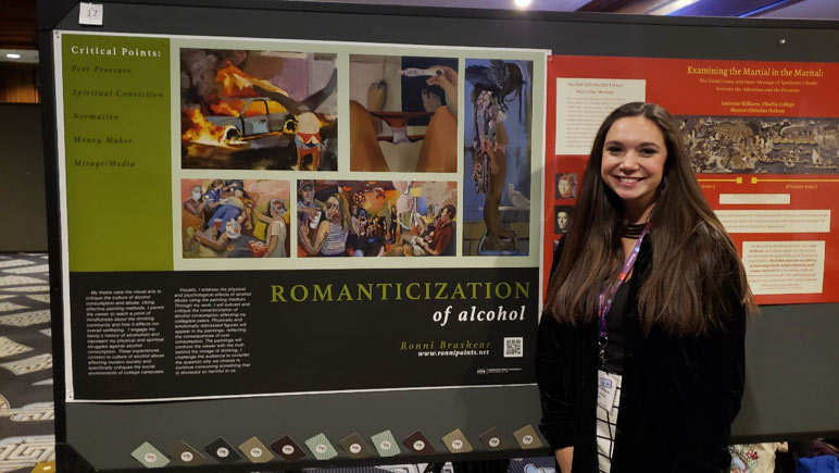 female student posing to the right of a display board