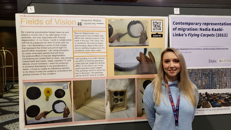 female student posing to the right of a display board