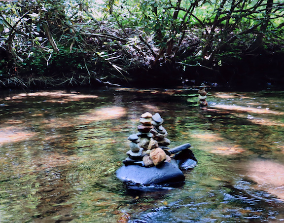 Picture of a stream and in the middle, rocks stacked on one another.