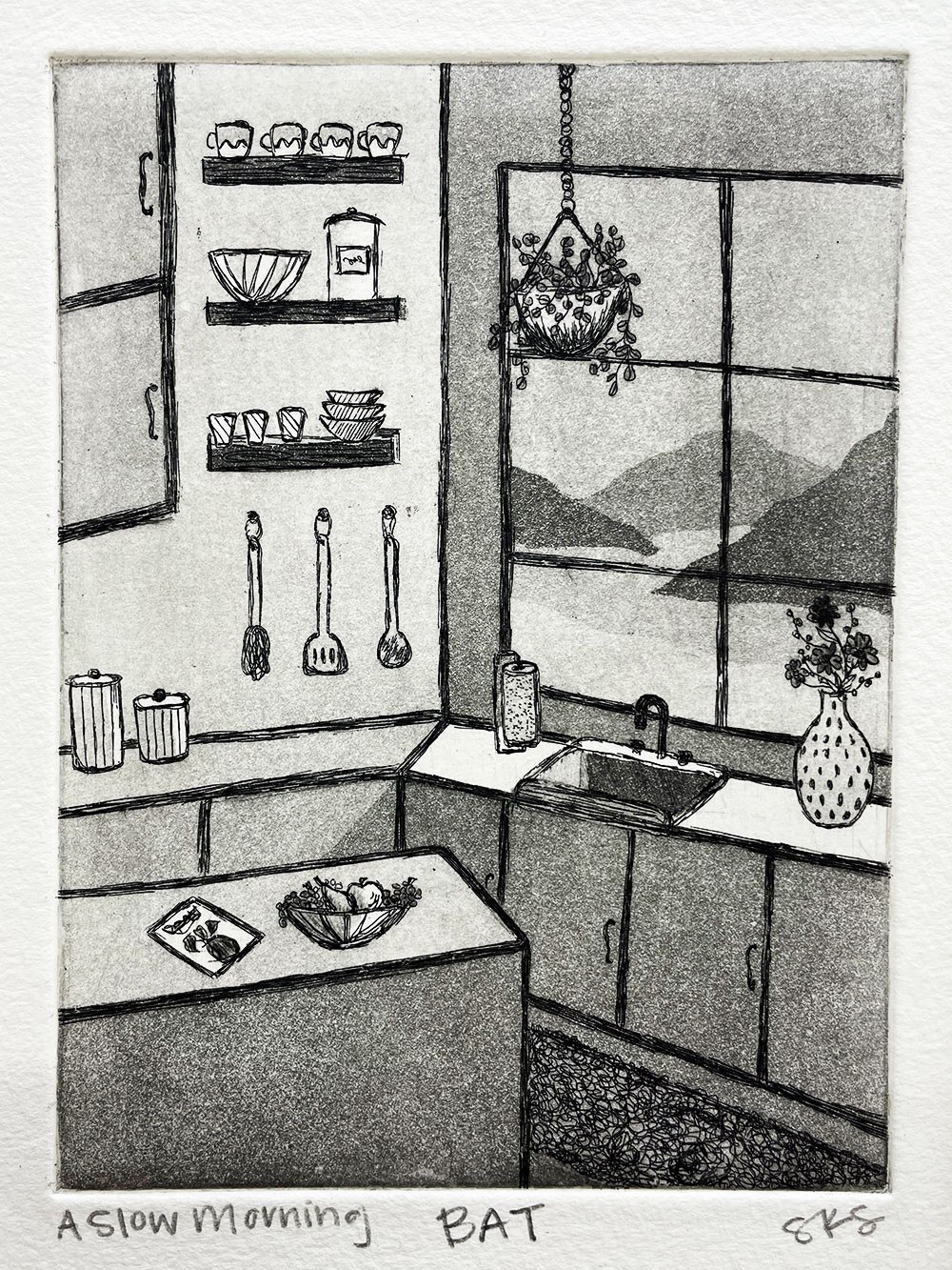 A black and white printed image of the corner of a kitchen overlooking the mountains. There is a flower pot, a bowl of fruit, a plant hanging, and shelves with cups and bowls. 