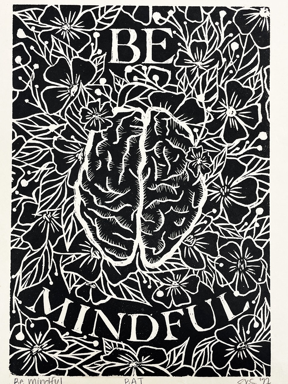 A printed image of a brain surrounded by flowers and leaves, with the words written "Be mindful".