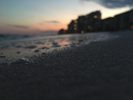 Color photograph of a close up image depicting sand and a beach at sunset.