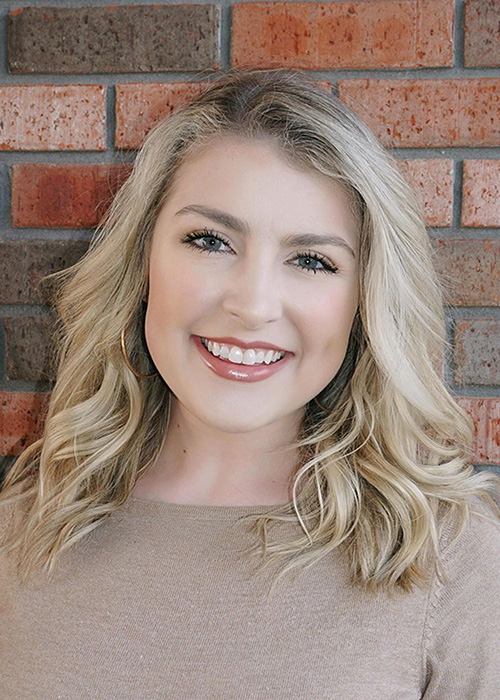 Savannah Crew headshot - tan shirt and brick backdrop