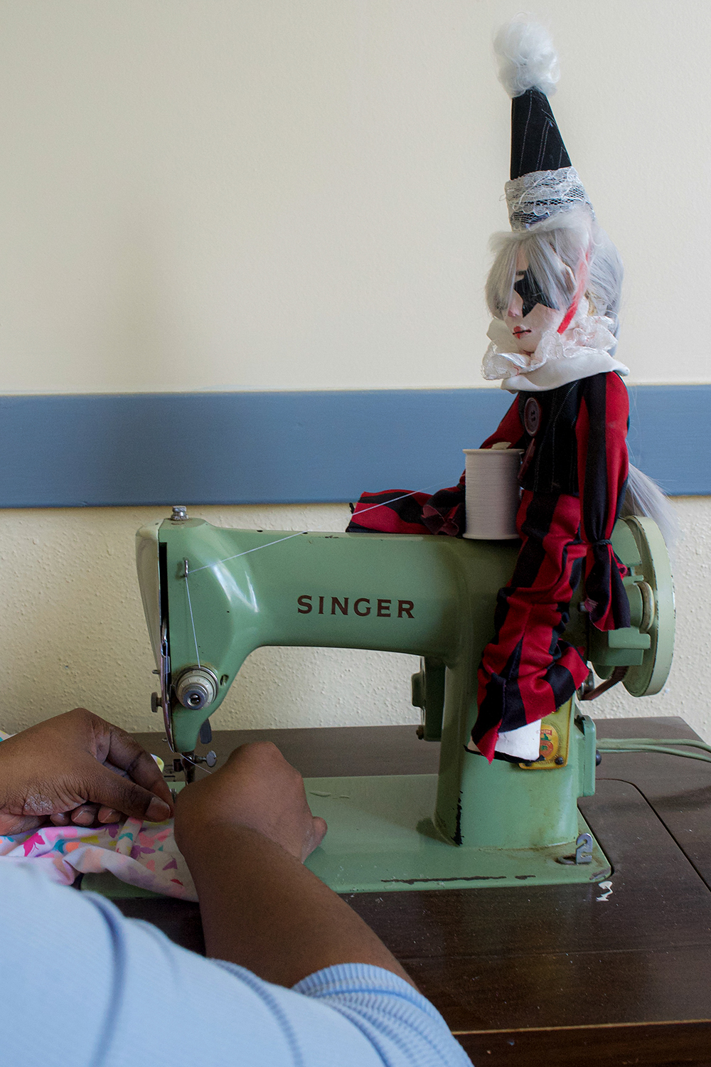 One of the artist's doll is sitting atop the sewing machine as the artist is working.