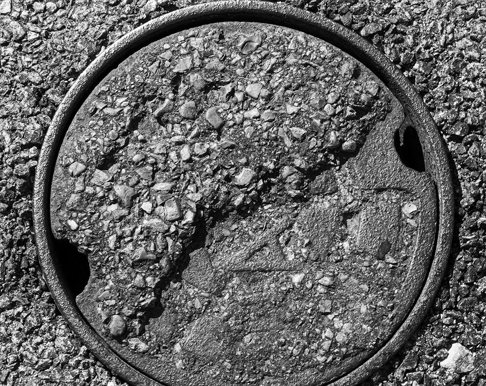 A black and white photographed image of the top of a sewage drain. 