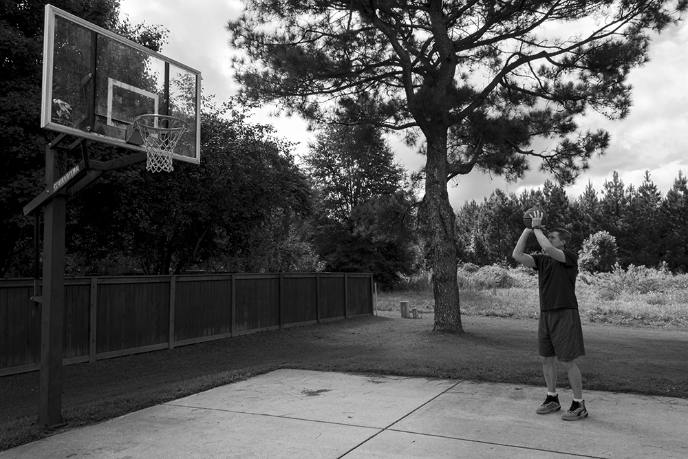 A black and white photographed image of a man throwing a basketball.