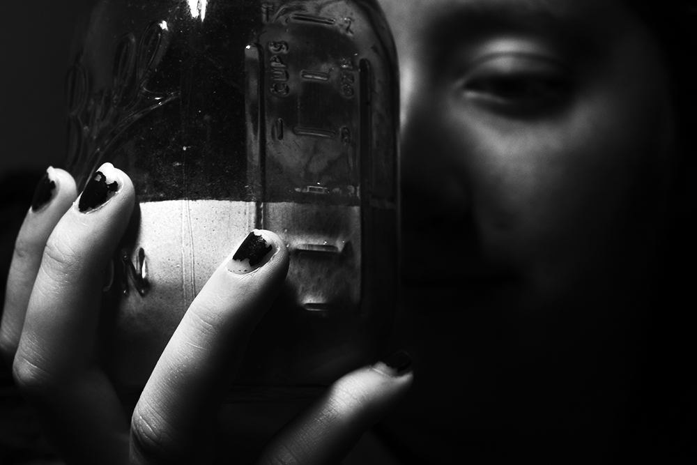A black and white photographed image of a person holding a jar
