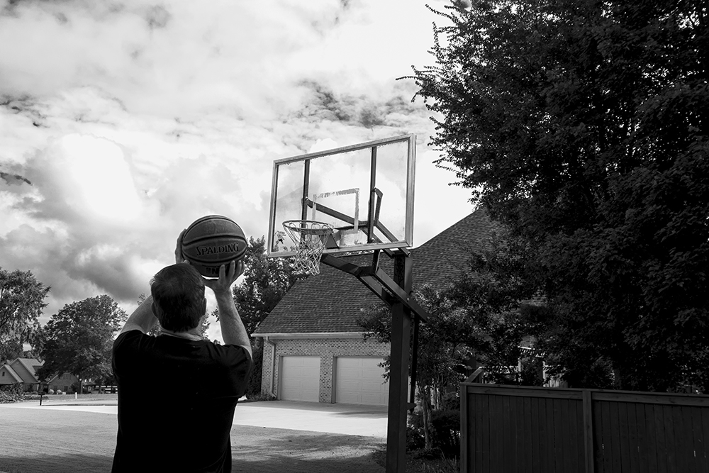 A black and white photographed image of a man throwing a basketball.