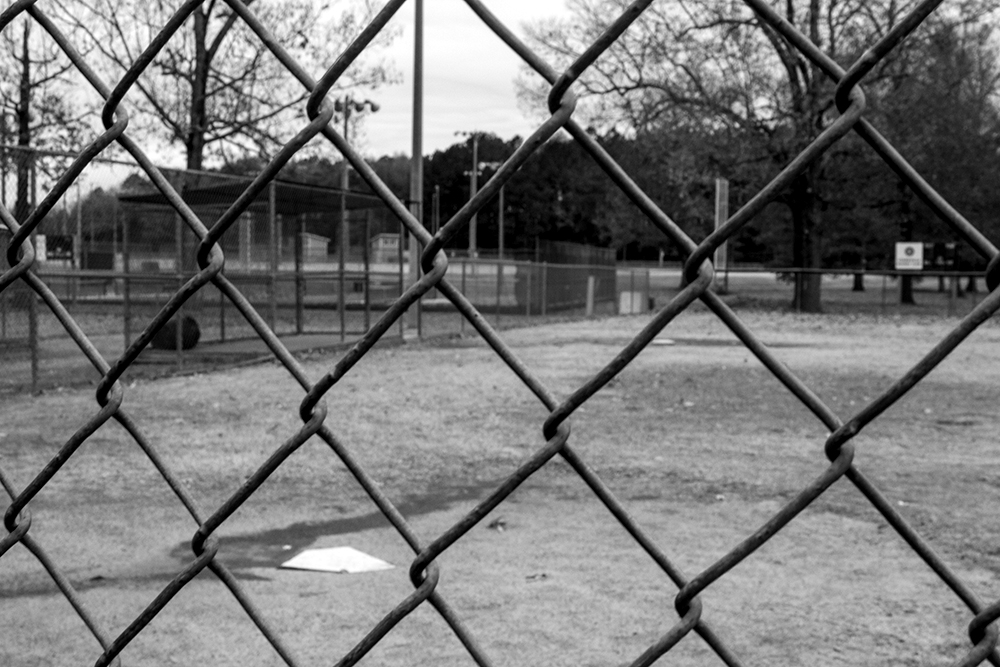 A black and white photographed image of a baseball field from behind the gate