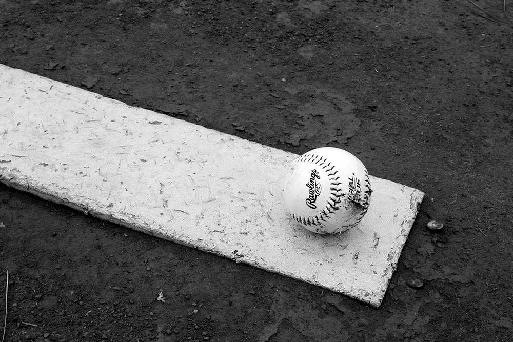 A black and white photographed image of a baseball resting on the pitchers mound.