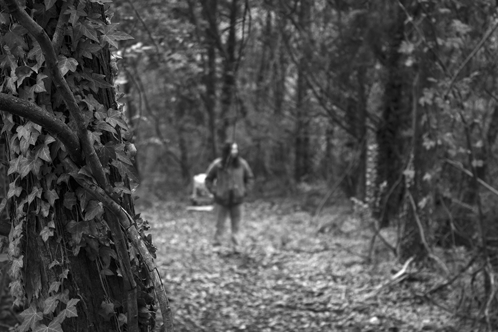 A black and white photographed image of a woman standing in the woods