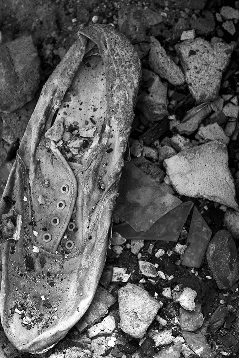 A black and white photographed image of a dirty shoe surrounded by rocks.