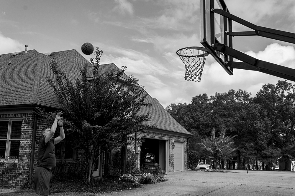 A black and white photographed image of a man throwing a basketball.