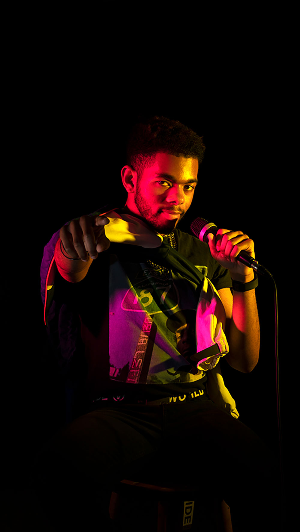 A photographed image of a man holding a microphone and pointing. 