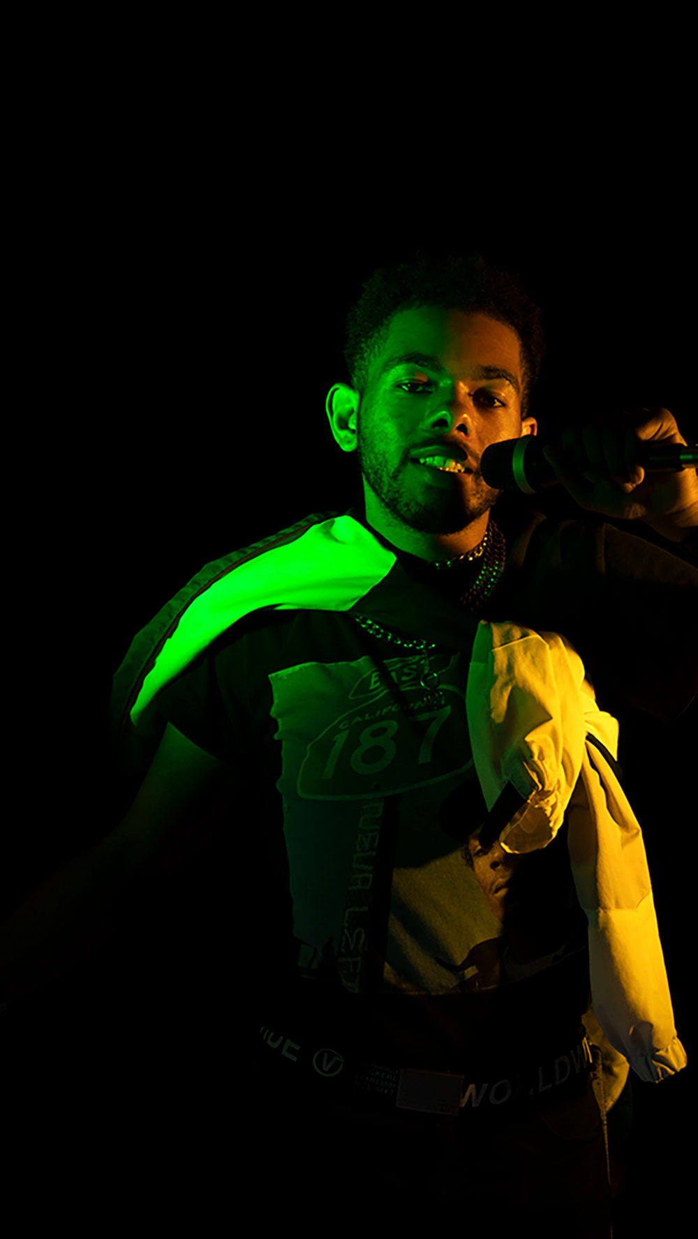 A photograph of a man singing into a microphone with a green light shining on him. 