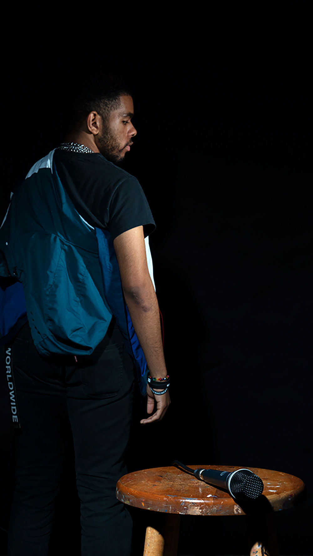 A photograph of a man standing with a microphone resting on a stool