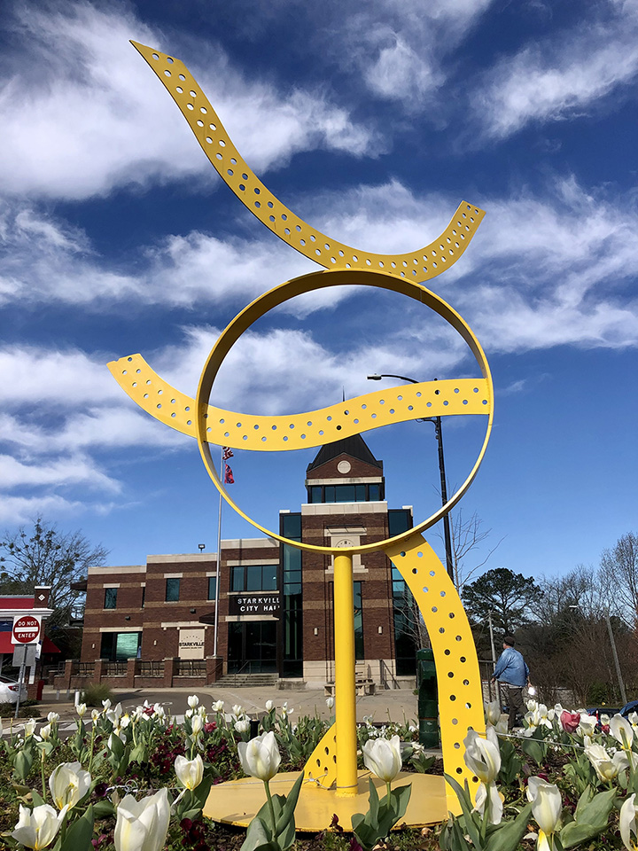 Metal sculpture painted yellow standing outdoors.