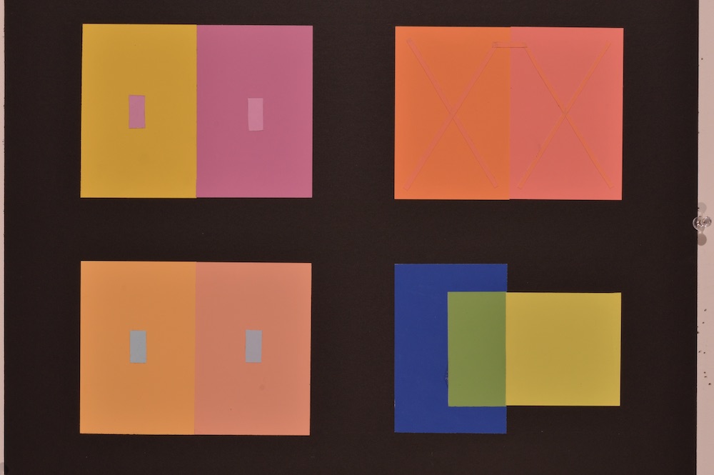 Color interaction study in which various strips of paper are set on top of color swatches, they appear to all be the same color because of the interaction with contrasting color. This interaction is blue. 