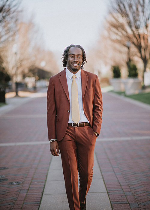 Willie Griffin in suit walking on brick walkway on campus