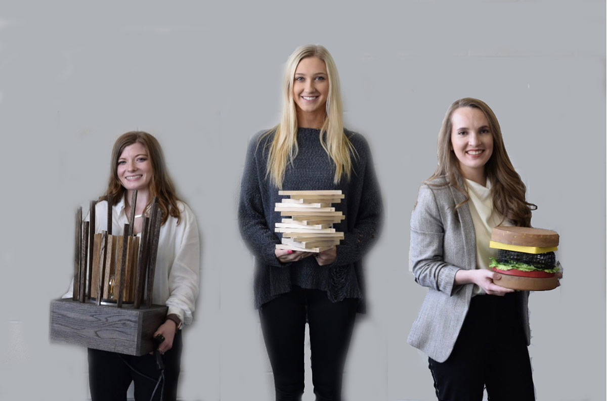 three females holding lamp designs: left lamp is a wooden base with wooden sticks sticking up a circular pattern; middle lamp is books stacked on top of each other in a zigzag pattern; right lamp looks like a hamburger in a bun with cheese, lettuce and tomato