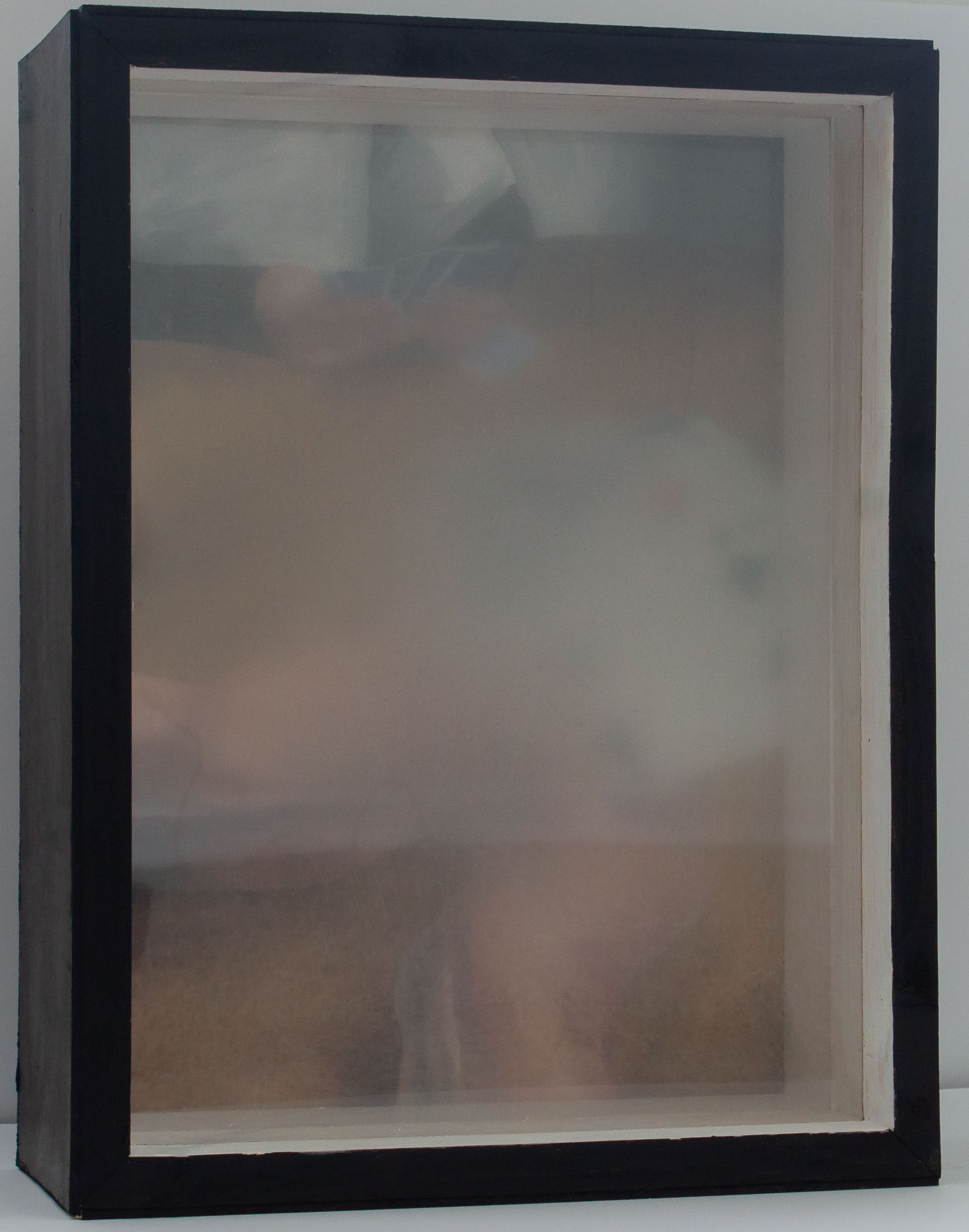 A box with a painting in the back and treated plexiglass panels interfering with the view of the painting. The painting shows an older person’s hands holding playing cards. There is another person sat across from the hands playing the game as well. Both panels are in front of the painting. The front most panel of plexiglass is fuzzy and smooth. The back panel of plexiglass is rough, scratched, and blurry. Both panels are blurry more in the center and fade out.