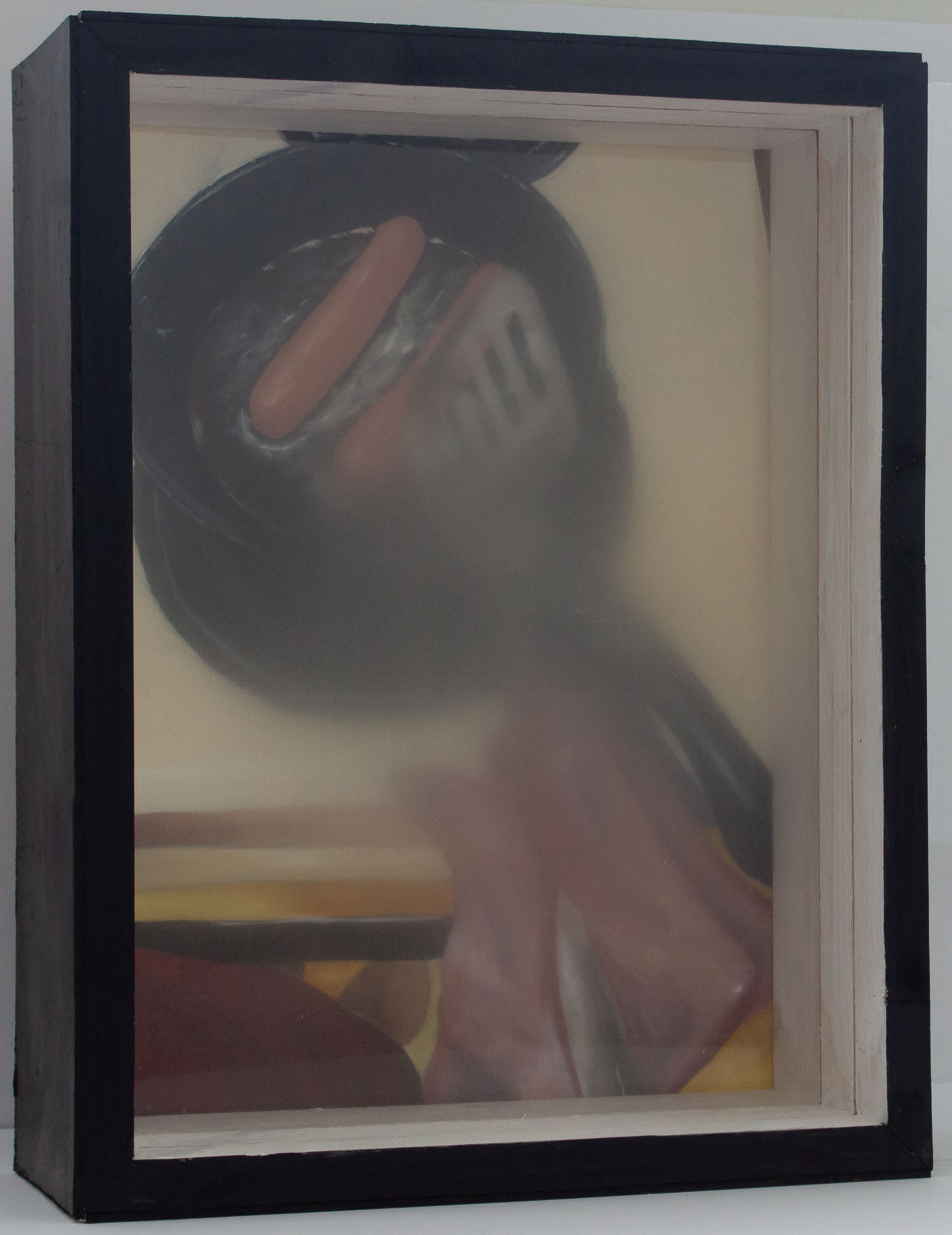A box with a painting in the back and treated plexiglass panels interfering with the view of the painting. The painting shows an older person’s hand as they cook two hotdogs on a skillet. The person is holding a spatula. They are wearing a red shirt. The stove top surrounding the eye being used is visible. The front panel is slid out from the box. The back panel is still obscuring the painting. The back panel of plexiglass is rough, scratched, and blurry. Both panels are blurry more in the center and fade out.