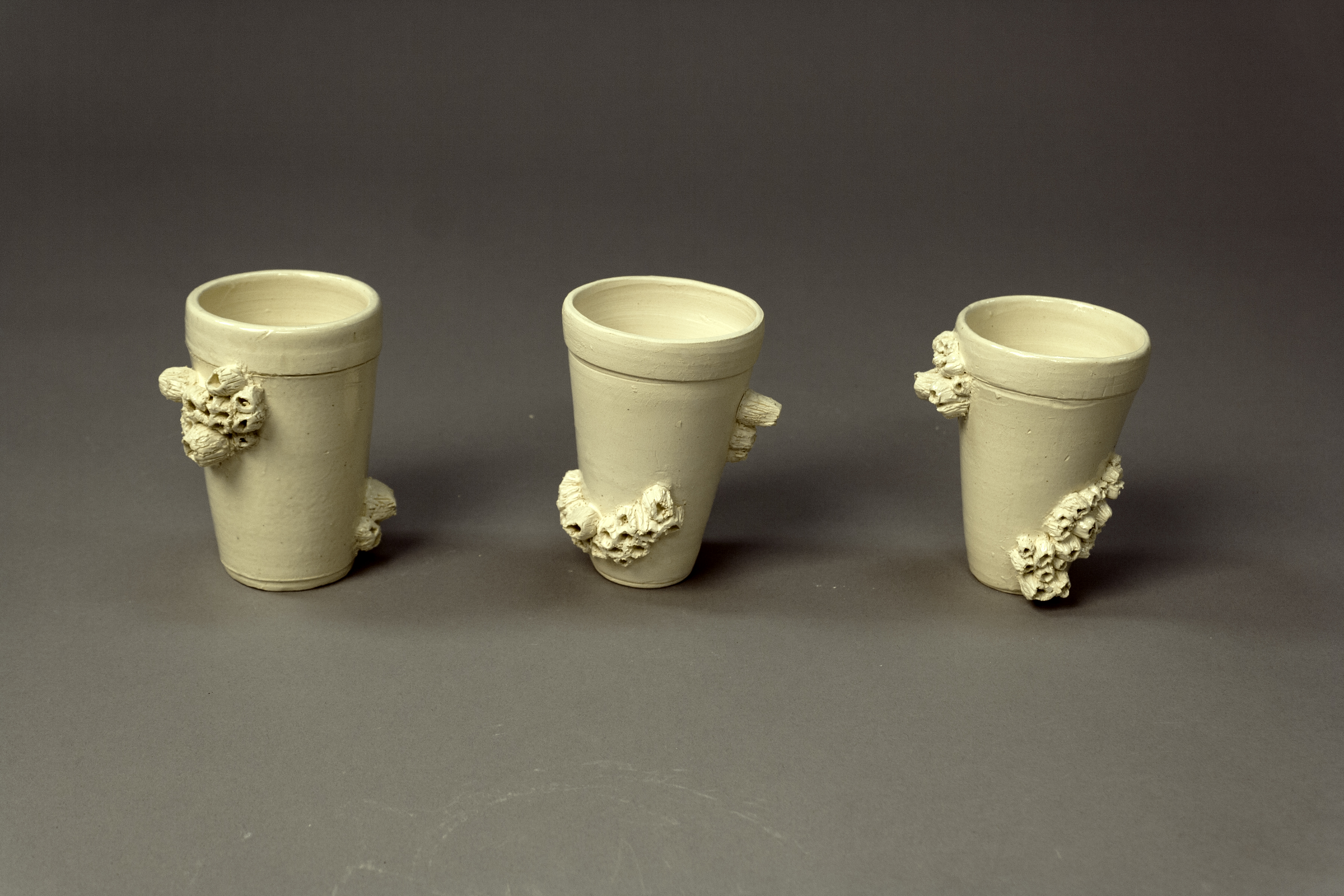 3 ceramic cups that look like styrofoam cups with barnacles growing all over them. 