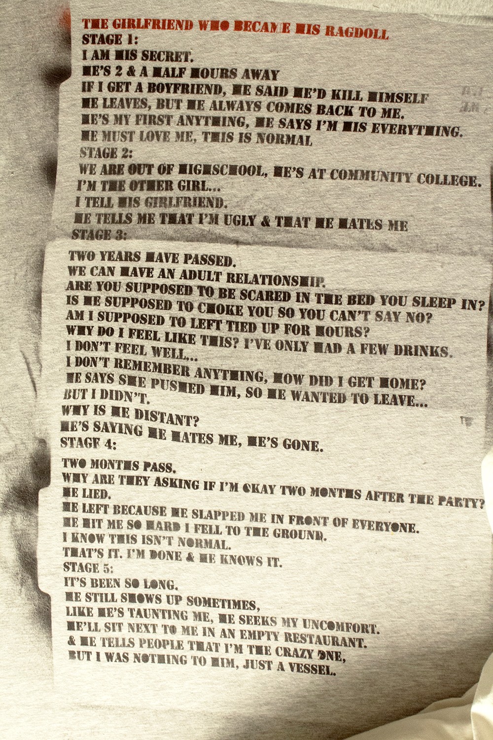 detail shot of poem stenciled on bedsheet: THE GIRLFRIEND WHO BECAME HIS RAGDOLL STAGE 1: I AM HIS SECRET. HE’S 2 & A HALF HOURS AWAY IF I GET A BOYFRIEND, HE SAID HE’D KILL HIMSELF HE LEAVES, BUT HE ALWAYS COMES BACK TO ME. HE’S MY FIRST ANYTHING, HE SAYS I’M HIS EVERYTHING. HE MUST LOVE ME, THIS IS NORMAL STAGE 2: WE ARE OUT OF HIGHSCHOOL, HE’S AT COMMUNITY COLLEGE. I’M THE OTHER GIRL... I TELL HIS GIRLFRIEND. HE TELLS ME THAT I’M UGLY & THAT HE HATES ME STAGE 3: TWO YEARS HAVE PASSED. WE CAN HAVE AN ADULT RELATIONSHIP. ARE YOU SUPPOSED TO BE SCARED IN THE BED YOU SLEEP IN? IS HE SUPPOSED TO CHOKE YOU SO YOU CAN’T SAY NO? AM I SUPPOSED TO LEFT TIED UP FOR HOURS? WHY DO I FEEL LIKE THIS? I’VE ONLY HAD A FEW DRINKS. I DON’T FEEL WELL… I DON’T REMEMBER ANYTHING, HOW DID I GET HOME? HE SAYS SHE PUSHED HIM, SO HE WANTED TO LEAVE… BUT I DIDN’T. WHY IS HE DISTANT? HE’S SAYING HE HATES ME, HE’S GONE. STAGE 4: TWO MONTHS PASS.  WHY ARE THEY ASKING IF I’M OKAY TWO MONTHS AFTER THE PARTY? HE LIED. HE LEFT BECAUSE HE SLAPPED ME IN FRONT OF EVERYONE. HE HIT ME SO HARD I FELL TO THE GROUND. I KNOW THIS ISN’T NORMAL. THAT’S IT. I’M DONE & HE KNOWS IT. STAGE 5: IT’S BEEN SO LONG. HE STILL SHOWS UP SOMETIMES, LIKE HE’S TAUNTING ME, HE SEEKS MY UNCOMFORT. HE’LL SIT NEXT TO ME IN AN EMPTY RESTAURANT. & HE TELLS PEOPLE THAT I’M THE CRAZY ONE, BUT I WAS NOTHING TO HIM, JUST A VESSEL.