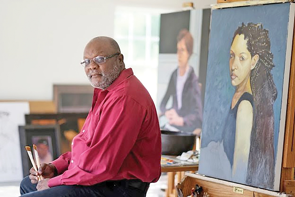 Photograph of artist Alex Bostic sitting in his studio in front of a painting.