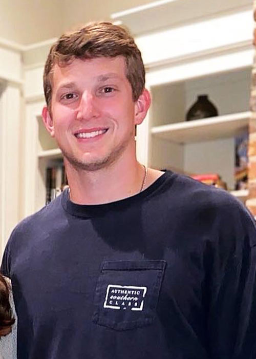 Colton Cox poses inside - shelves seen behind him - wearing dark shirt