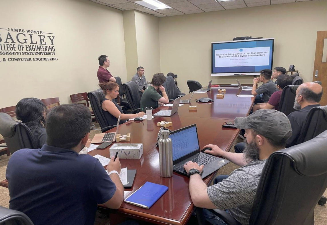 Presentation on how AI & Cyber Infrastructure is Revolutionizing Construction Management. Shows group sitting at conference table looking at presentation on tv screen