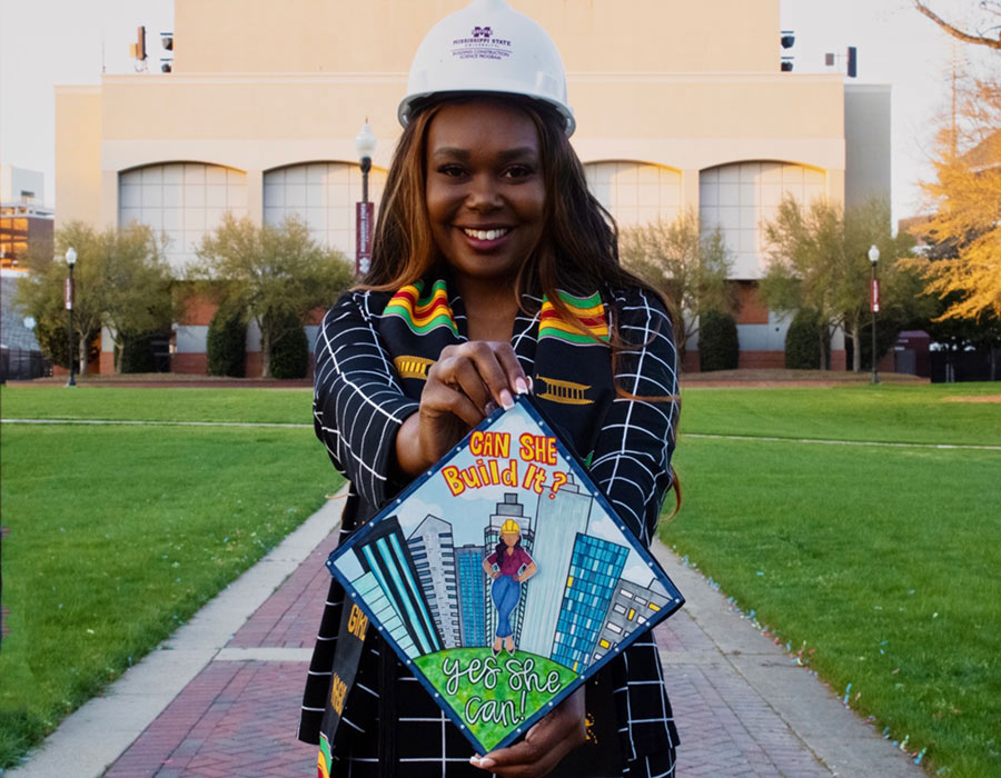Jazmine Melton wearing a Mississippi State construction hat while holding her decorated graduation cap.