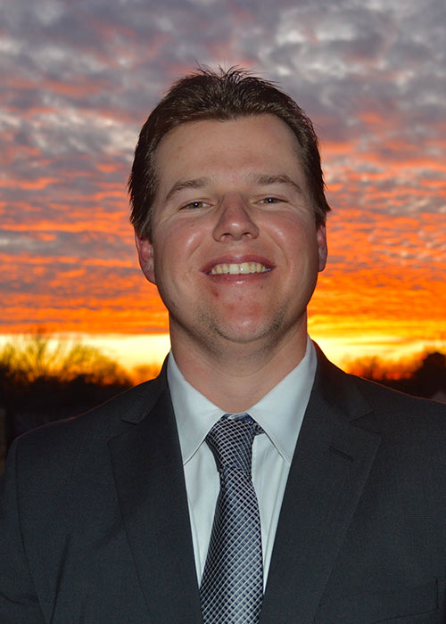 Owen McCallum headshot wearing suit and tie with sunset in background