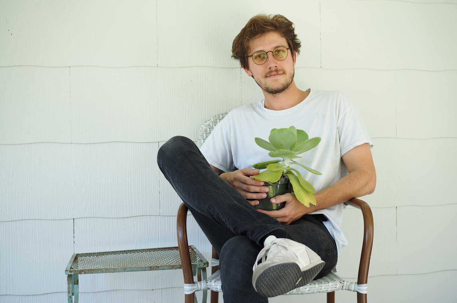 Aubrey Pohl sits outside on a front porch with leg crossed and holding a green leaf plant 