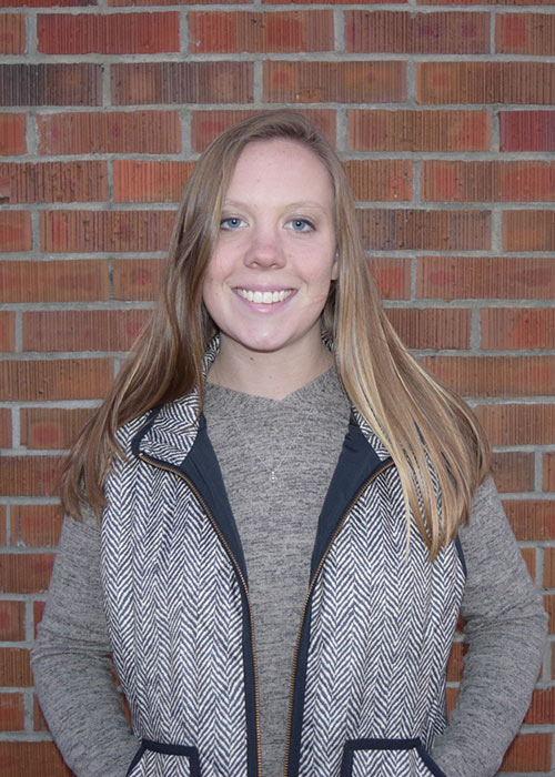 Jalyn Wallin headshot - against brick wall - wearing gray shirt and gray vest