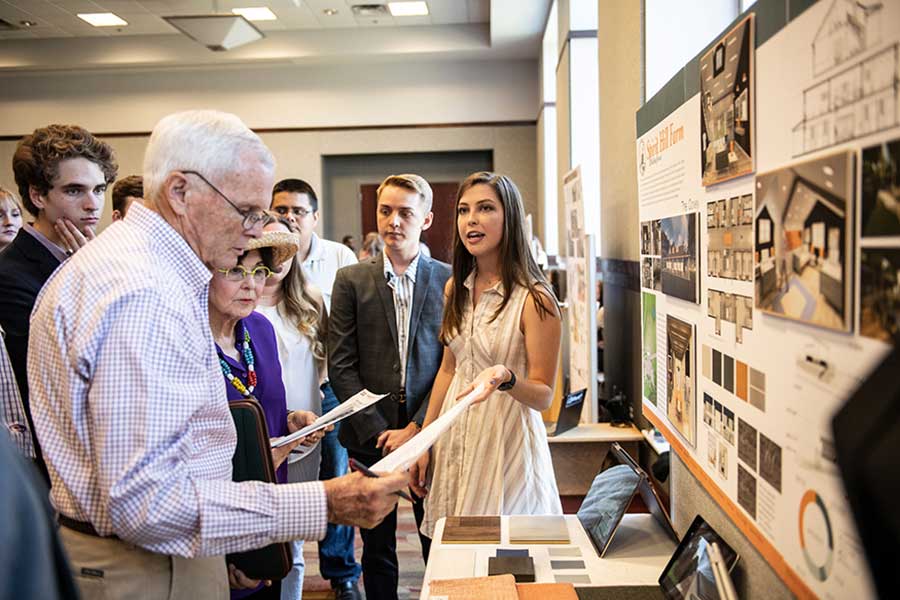 Olivia A. Baker, right, hands a paper to Bob and Sheryl Bowen as others look on - project board behind Olivia