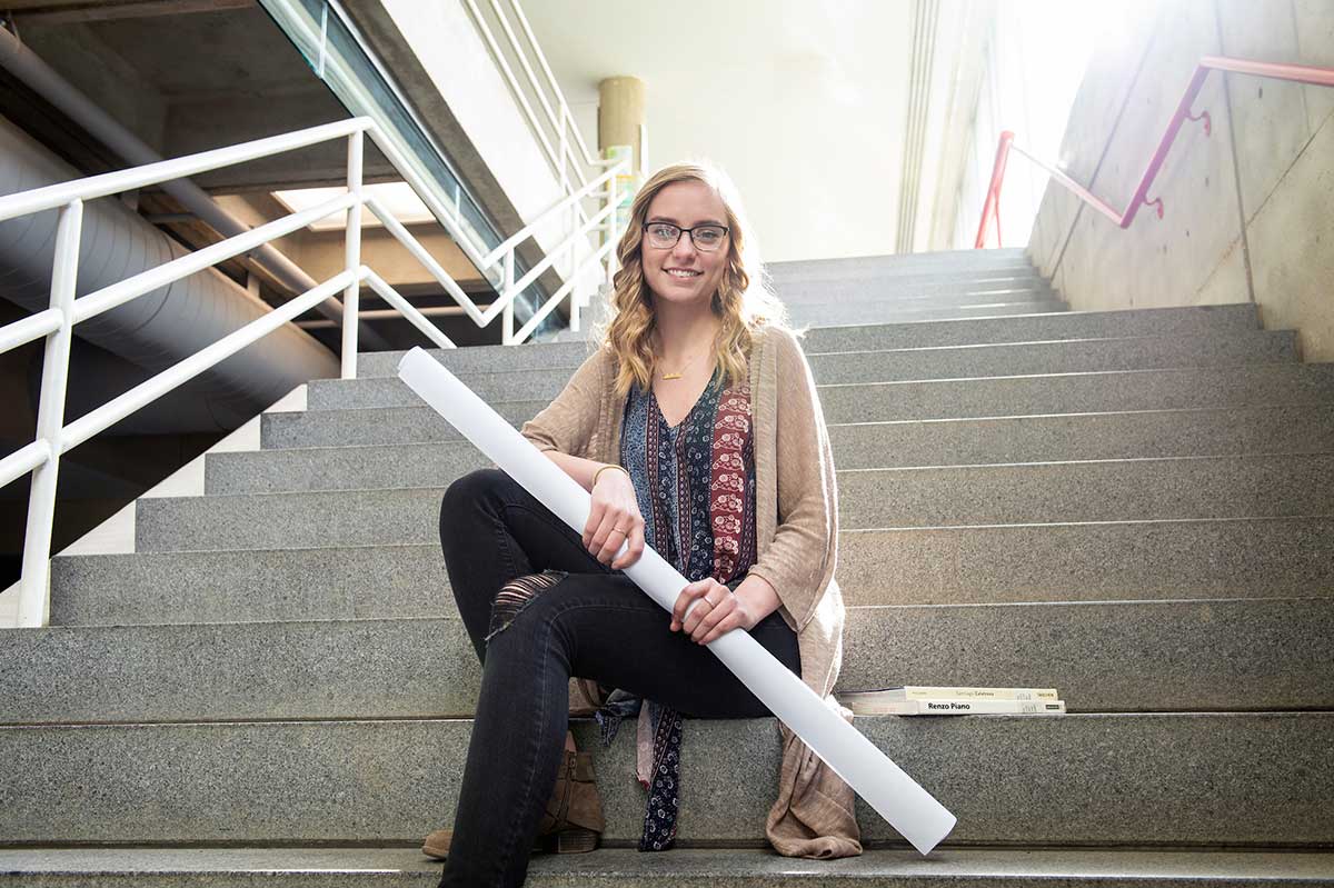 Sarah Hoing poses with architecture plans on the main steps inside Giles Hall, Mississippi State University, Starkville campus  (photo by Megan Bean / © Mississippi State University)