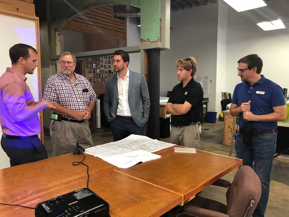 Anthony Kendrick, left, presented at GCCDS to four standing around table with projector behind them and a map on the table