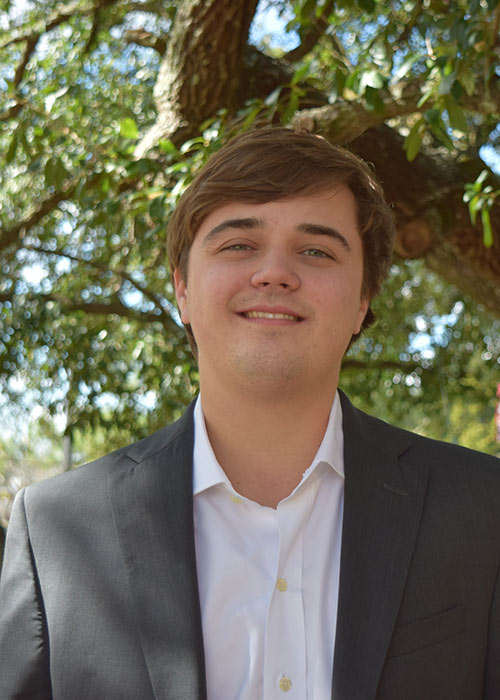 Case Woodward headshot - wearing suit with tree/leaves in background